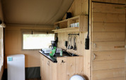 Interieur van een safaritent met houten kasten en keuken op Camping de Heerlijkheid Vorenseinde, Nederland.