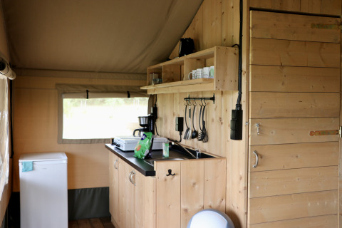 Interno di una tenda safari con mobili in legno e cucina al Camping de Heerlijkheid Vorenseinde, Paesi Bassi.