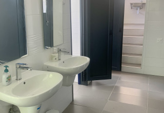Badkamer in een safaritent met dubbele lavabo's, spiegels, zeep, afvalbak en open klapdeuren.