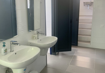 Baño de una tienda safari con dos lavabos, espejos y puertas de cabina oscuras parcialmente abiertas.