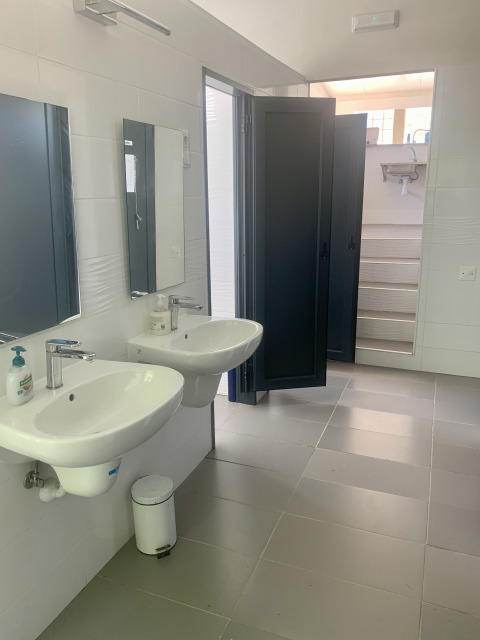 Bagno di tenda safari con due lavandini, specchi, sapone, cestino e porte doccia scorrevoli aperte.