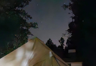 Foto van een safaritent bij nacht, omgeven door bomen onder een heldere sterrenhemel en gebouwen.