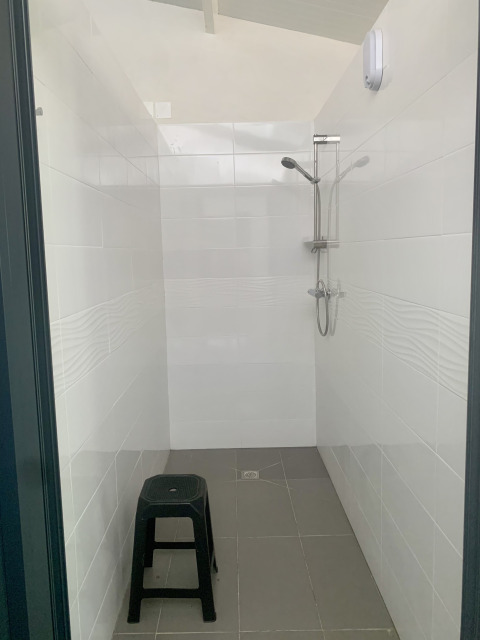 Afbeelding van een eenvoudige douche in een safaritent met een zwart plastic krukje en witte tegels.