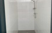 Afbeelding van een eenvoudige douche in een safaritent met een zwart plastic krukje en witte tegels.