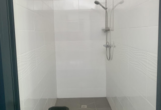 Afbeelding van een eenvoudige douche in een safaritent met een zwart plastic krukje en witte tegels.