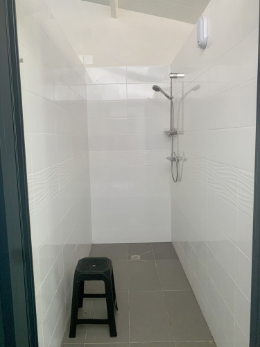Photo of a basic shower inside a safari tent, featuring a black plastic stool and white tiled walls.
