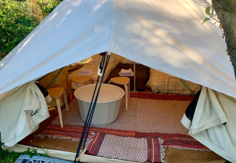 Safari-Glamping-Zelt mit offener Vorderseite, Teppichen, kleinen Tischen und Betten bei Glamping de Cerveira.
