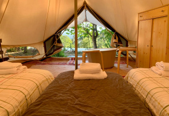 Interior de la tienda Oliveira Bell Standard en Glamping de Cerveira, Portugal, con camas y bañera visible.