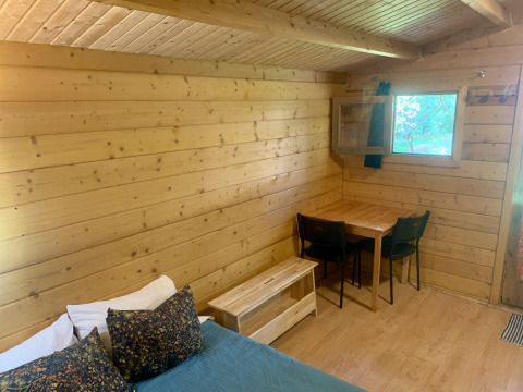 Interior de la Azalea Cabin en Glamping de Cerveira, Portugal, con paredes de madera, mesa y ventana abierta.