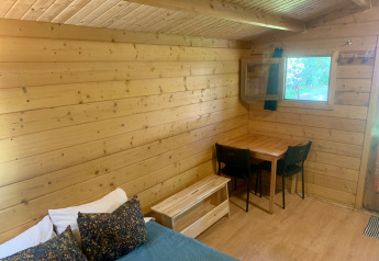 Interior de la Azalea Cabin en Glamping de Cerveira, Portugal, con paredes de madera, mesa y ventana abierta.