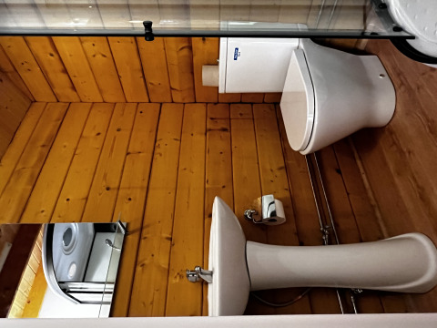 Baño con paredes de madera, inodoro y lavabo blancos en la Azalea Cabin de Glamping de Cerveira, Portugal.