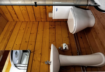 Bagno con pareti in legno, wc e lavabo bianchi nella Azalea Cabin al Glamping de Cerveira, Portogallo.