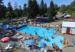 Feriecampister og familier nyder en solrig dag ved udendørs poolen på Vestbirk Camping med rutsjebane.