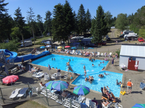 Families and campers enjoy a sunny day at Vestbirk Camping’s outdoor pool area with water slide and sun loungers.