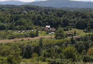 Panoramic view of a holiday park with glamping tents and cottages nestled in lush green countryside hills.