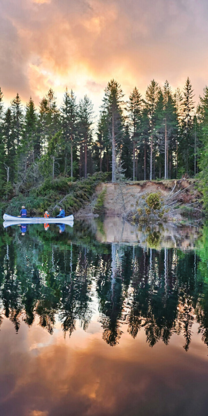 Due persone in canoa remano su un lago calmo al tramonto in un parco vacanze con glamping.