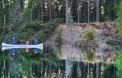 Due persone in canoa remano su un lago calmo al tramonto in un parco vacanze con glamping.