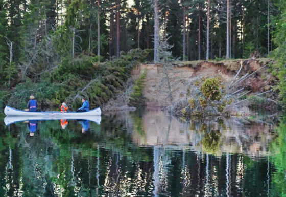Due persone in canoa remano su un lago calmo al tramonto in un parco vacanze con glamping.