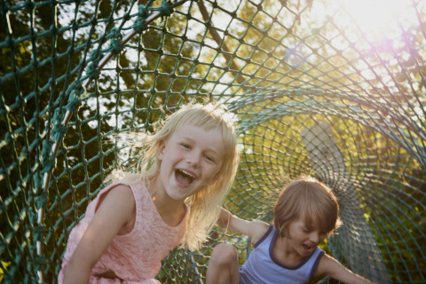 Dos niños felices jugando en un túnel de red bajo el sol en Vestbirk Camping, Dinamarca.