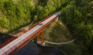 Foto aérea de un puente rojo sobre un río y bosque cerca de Østbirk, Dinamarca, con ciclistas cruzando.