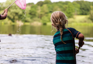 Dos niños juegan junto al lago en Vestbirk Camping, Dinamarca, rodeados de naturaleza verde exuberante.
