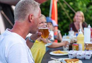 Man geniet van een drankje met familie aan tafel bij Vestbirk Camping in Denemarken, ontspannen sfeer.