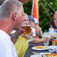 Man enjoys a drink with family around a table at Vestbirk Camping in Denmark, relaxed outdoor meal.