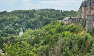 Vista de colinas verdes, un castillo cerca de Kyllburg, Alemania, y una iglesia lejana bajo un cielo nublado.