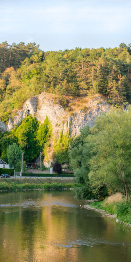 Rivière, falaise et arbres près d’un parc de vacances avec hébergements glamping. Scène estivale paisible.