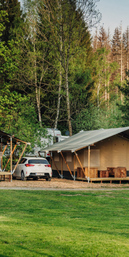 Cabaña y coche en el parque vacacional Camp Kyllburg, rodeados de bosque en Renania-Palatinado, Alemania.