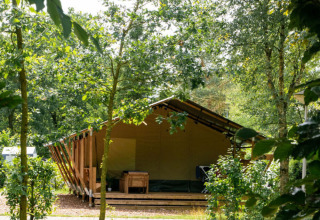 Glampingtent in een vakantiepark, omringd door bomen en groen, ideaal voor een ontspannen verblijf.