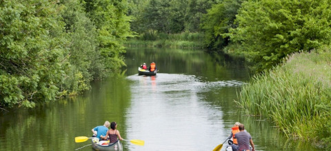 People in canoes paddling along a tranquil river surrounded by lush greenery at Vestbirk Camping, Denmark.