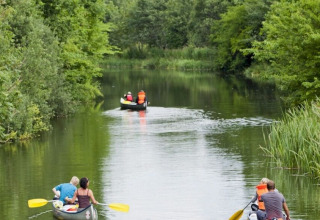 People in canoes paddling along a tranquil river surrounded by lush greenery at Vestbirk Camping, Denmark.