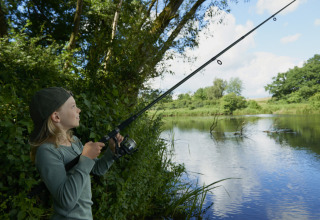 Child fishing by a tree-lined lake at Vestbirk Camping holiday park in the Capital Region of Denmark.