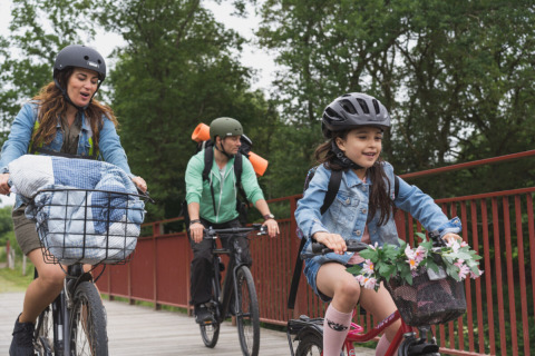 Gezin fietst met helmen over een brug bij Vestbirk Camping, Denemarken, omgeven door groene natuur.