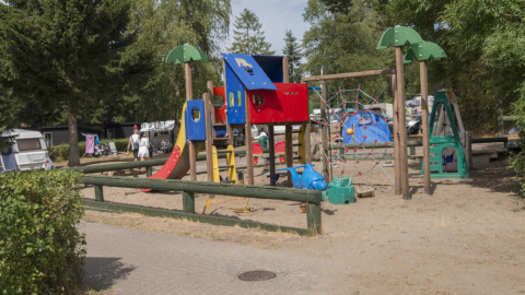 Playground with colorful climbing frame and slide at Vestbirk Camping, surrounded by trees and tents.