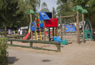 Legeplads med farverigt klatrestativ og rutsjebane på Vestbirk Camping, omgivet af træer og telte.