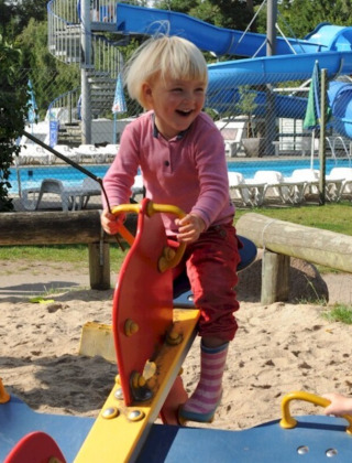 Kinderen spelen op een wip bij Vestbirk Camping speeltuin, met zwembad en glijbaan op de achtergrond.