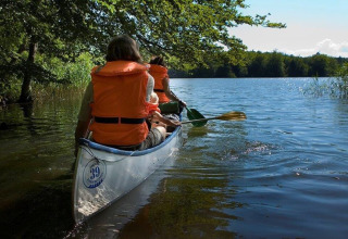 Zwei Personen paddeln in einem Kanu auf einem ruhigen See bei Østbirk, Dänemark, mit Schwimmwesten.