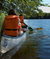 Dos personas reman en una canoa sobre un lago tranquilo cerca de Østbirk, Dinamarca, usando chalecos salvavidas.