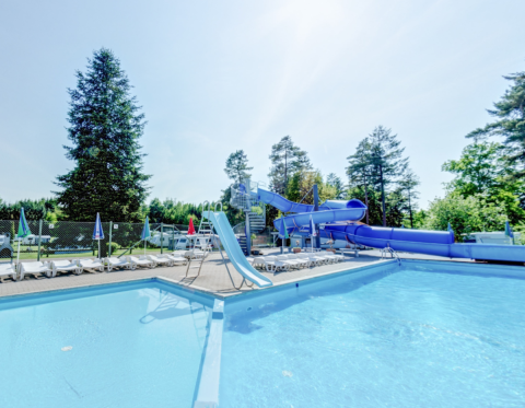 Udendørs swimmingpool med liggestole og stor blå vandrutsjebane ved Vestbirk Camping i Danmark.