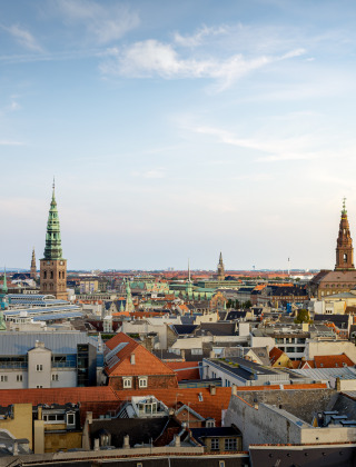 Panoramablick über die Dächer von Kopenhagen mit markanten Kirchtürmen und Altstadtgebäuden im Licht.
