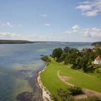 Vista panorámica de una bahía, jardines, iglesia y parque de vacaciones con glamping junto al agua y pueblo.