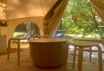 Intérieur de la tente safari Laurelia XL Family Tent à Glamping de Cerveira avec tables, chaises et verdure.