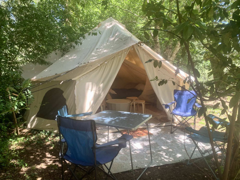 Tienda safari Laurelia XL Family Tent con entrada abierta, sillas al aire libre y mesa bajo los árboles.