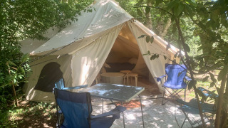 Safari tent Laurelia XL Family Tent met open ingang, buitenstoelen en tafel onder schaduwrijke bomen.