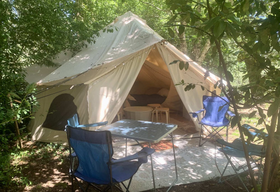 Safari tent Laurelia XL Family Tent met open ingang, buitenstoelen en tafel tussen de schaduwrijke bomen.