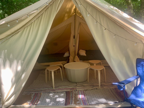 Interior de la tienda Laurelia XL Family Tent con mesas, taburetes y alfombras, en Glamping de Cerveira, Portugal.