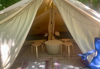Interior de la tienda Laurelia XL Family Tent con mesas, taburetes y alfombras, en Glamping de Cerveira, Portugal.