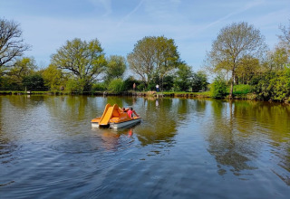 Barca a pedali con scivolo arancione su lago a Feather Down La Flocellière en Vendée, Pays de la Loire, Francia, al sole.